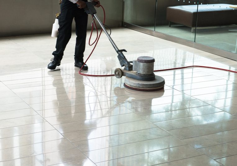 Building Maintenance, Cleaning, Floor Polishing. A worker is polishing a tile floor to make it shine and clean. The worker uses a polisher machine to get the job done. Building and facility maintenance is an ongoing chore.